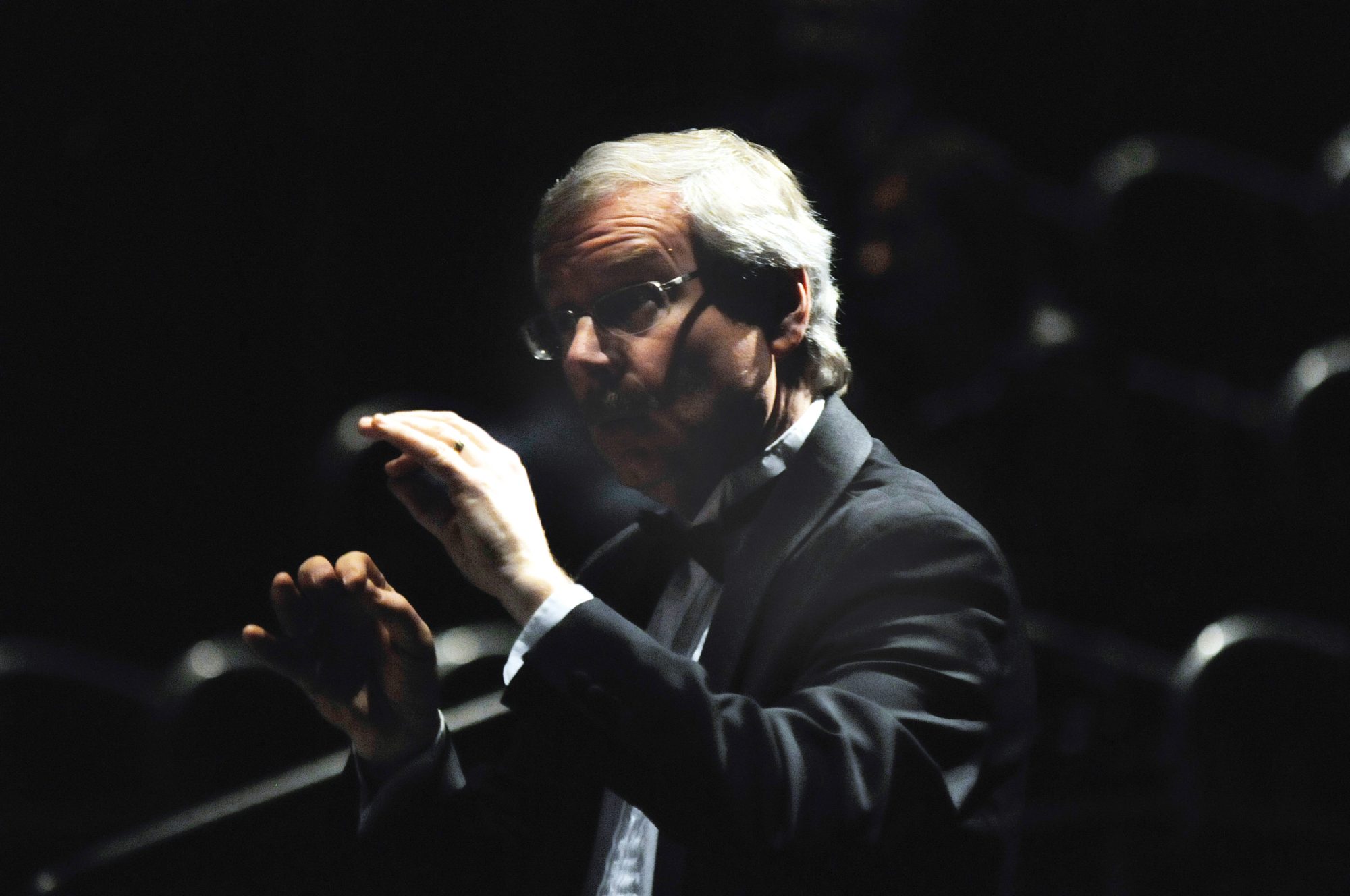 A band director conducting under stage lights, photographed by Richard Anseeuw